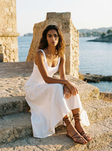 Load image into Gallery viewer, THE TARA handcrafted leather strappy sandal in cream on woman in whited seated on stone steps water backdrop — LUXUL COLLECTIVE
