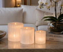 Load image into Gallery viewer, Three hand-carved selenite candle holders glowing on a marble table in a living room — THE NURA — LUXUL COLLECTIVE